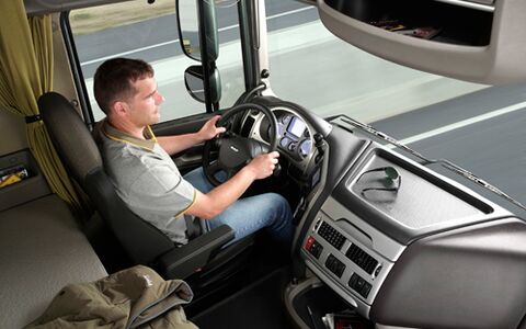 Blick von schrägoben rechts auf einen jungen LKW-Fahrer un seinen Arbeitsplatz hinter dem Lenkrad